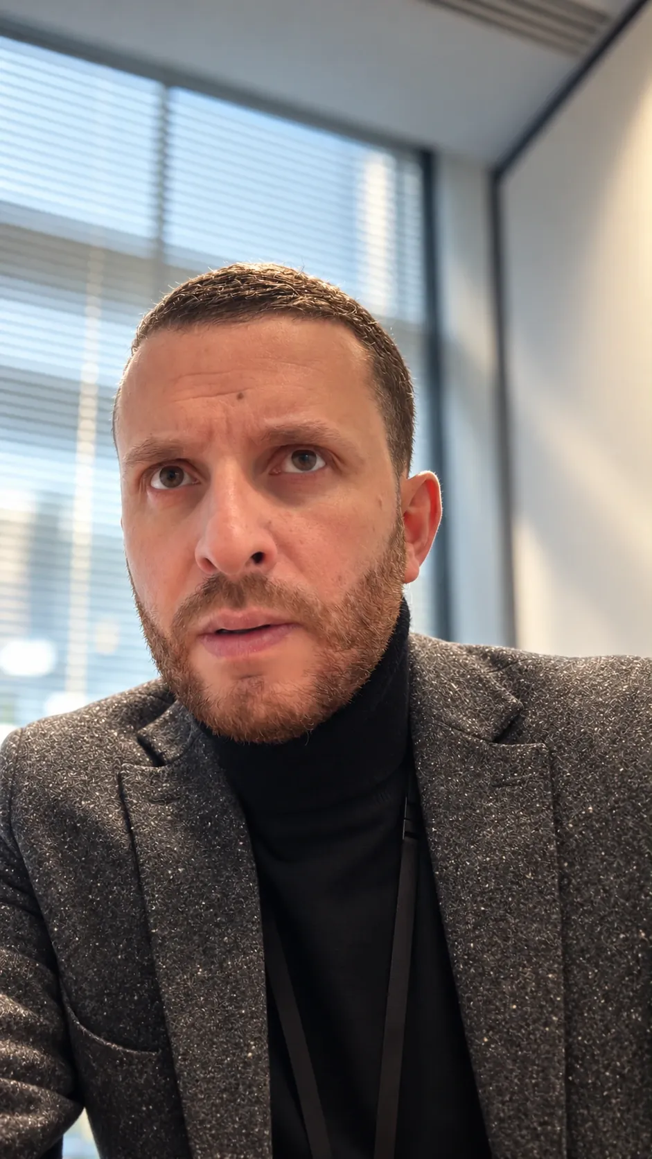 Bilal Nedman en veste grise et col roulé